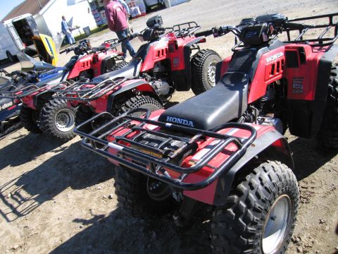 1991 Ford LTD Crown Victoria - Several red Honda ATVs are parked in a line on a dirt surface.