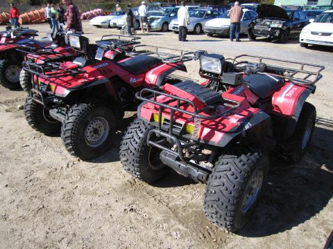 1991 Ford LTD Crown Victoria - Multiple red Honda all-terrain vehicles are lined up on a dirt lot, with several cars visible in the background.