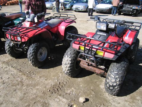 1991 Ford LTD Crown Victoria - Two red ATVs are parked on a dirt lot, with other vehicles in the background.