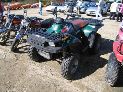 1991 Ford LTD Crown Victoria - A green Polaris ATV is parked on a dirt lot next to motorcycles and cars.