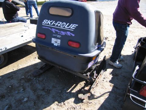 1991 Ford LTD Crown Victoria - A Ski-Roue snowmobile trailer is parked outdoors next to a trailer and a person.