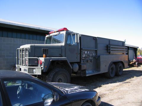 1991 Ford LTD Crown Victoria - A large military truck with a red emergency light on top is parked outdoors near a building.