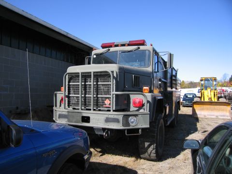 1991 Ford LTD Crown Victoria - A large military truck is parked next to a building, with other vehicles visible in the background.