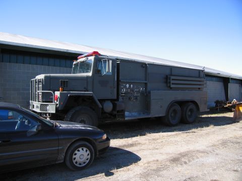 1991 Ford LTD Crown Victoria - A large green military truck is parked beside a black car in front of a building.