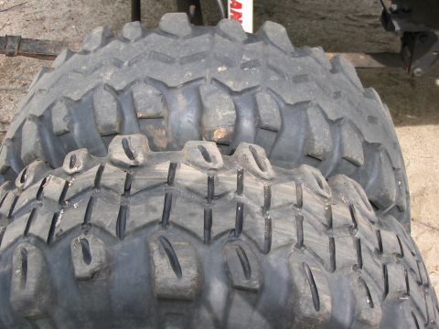 1985 Ford Bronco - Two large off-road tires are stacked, showing their deep, aggressive tread patterns. The "SUPERMOTORS" watermark is visible at the bottom r…