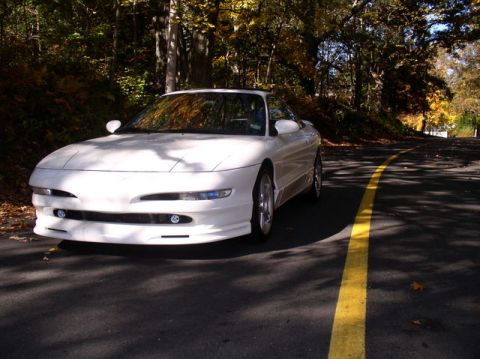 1996 Ford Probe - A white 1996 Ford Probe is parked on the side of a road, surrounded by trees with autumn foliage.