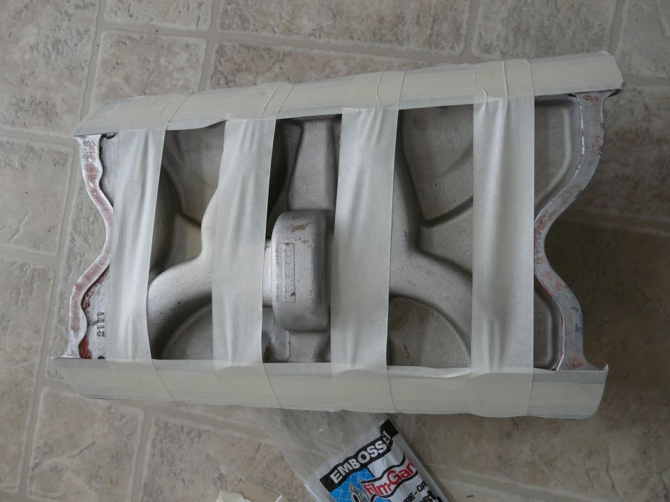 Aluminum intake manifold masked with tape for paint, resting on a tile floor
