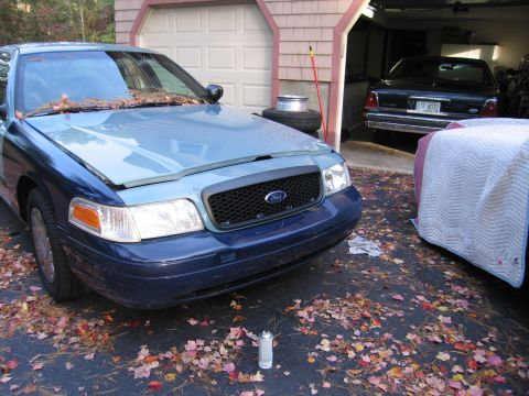1991 Ford LTD Crown Victoria - A 1991 Ford Crown Victoria LTD is seen from the front-three-quarter angle, with another vehicle covered in a white tarp in the background.