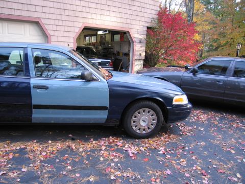 1991 Ford LTD Crown Victoria - Two cars are parked on a paved surface with fallen leaves.