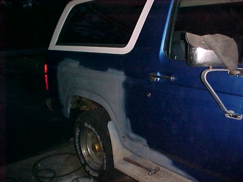 1985 Ford Bronco - A blue Ford Bronco shows primer on its rear quarter panel, indicating bodywork in progress.