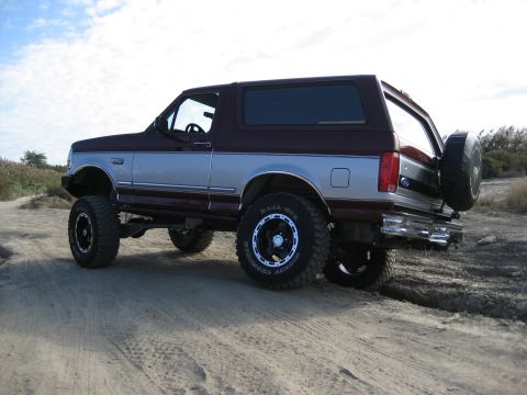 1996 Ford Bronco - This lifted 1996 Ford Bronco features a two-tone maroon and silver paint scheme and a spare tire mounted on the rear tailgate.