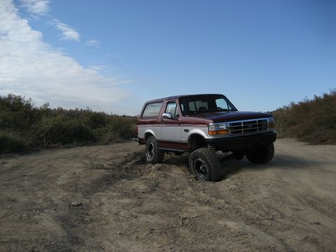 1996 Ford Bronco - A lifted Ford Bronco sits on a dusty trail under a clear blue sky.