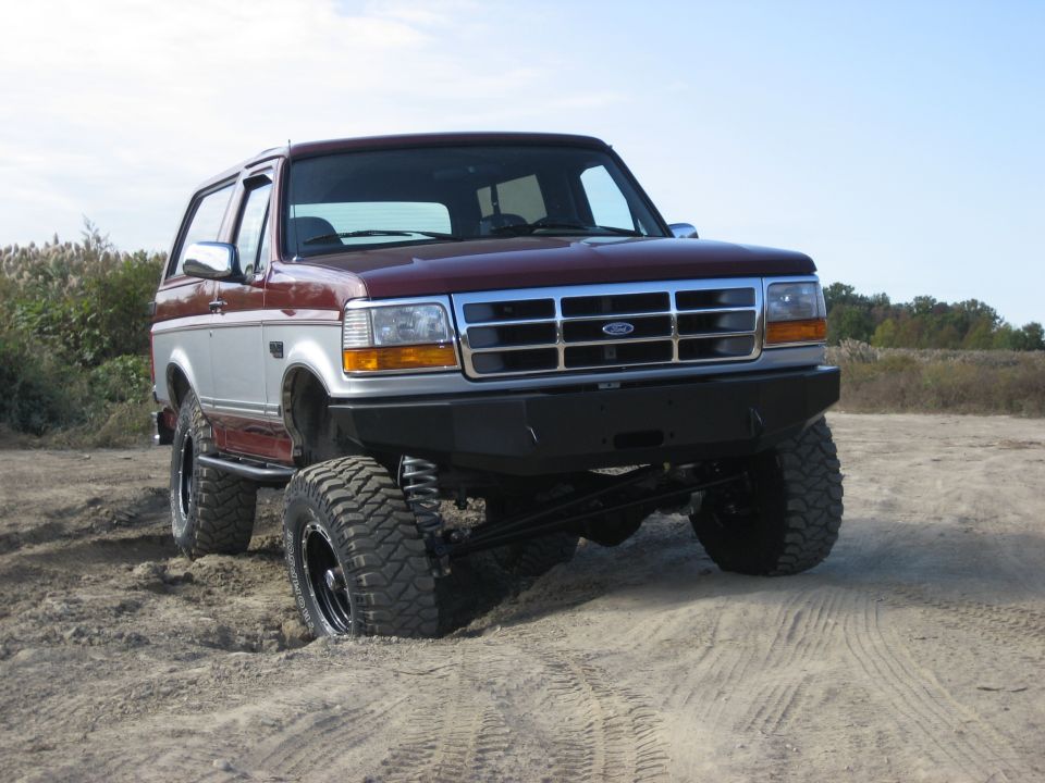 Maroon and silver Ford Bronco with aftermarket bumper and large tires stuck in sand