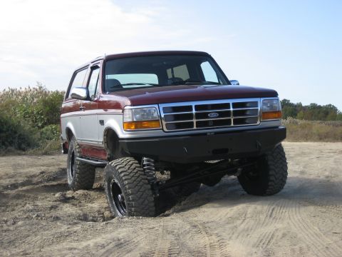 1996 Ford Bronco - This lifted 1996 Ford Bronco is shown in a three-quarter front view, navigating sandy terrain.