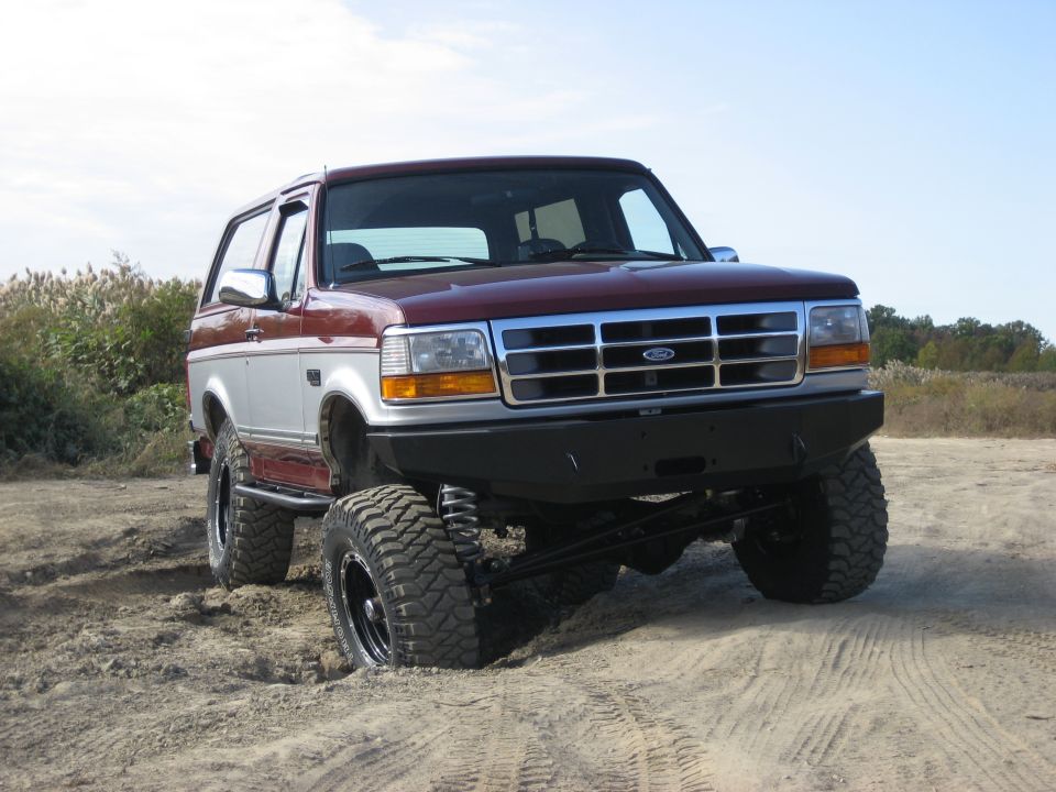 Red and silver lifted 1996 Ford Bronco in sand