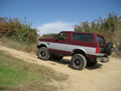 1996 Ford Bronco - 1996 Ford Bronco navigates a dusty trail under a clear blue sky, its off-road capability.