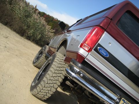 1996 Ford Bronco - This Ford Bronco features a two-tone paint scheme and aggressive off-road tires, seen here on a dirt road.