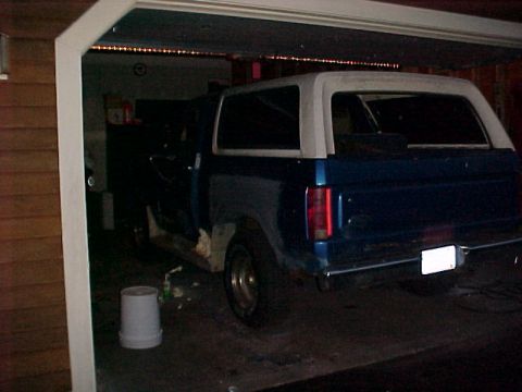 1985 Ford Bronco - Blue SUV with white top in garage, showing rear quarter panel damage.