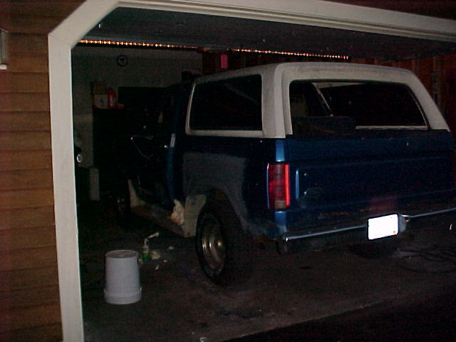 Rear view of a blue SUV with a white top parked in a garage. Body panels appear to be in disrepair