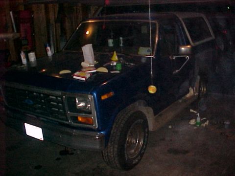1985 Ford Bronco - This blue SUV is parked indoors, with various items placed on its hood.