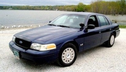2003 Ford Crown Victoria - A blue 2003 Ford Crown Victoria is parked on a gravel surface near a lake.