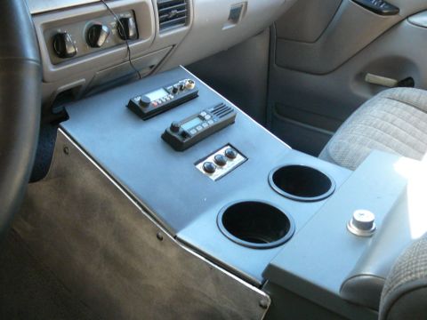 1988 Ford Bronco - Custom-fabricated gray center console mounted between the front seats of a Ford truck interior, holding two radios with LCD displays, a thr…