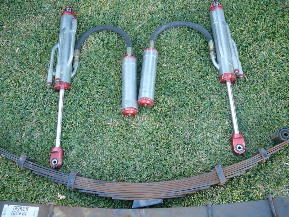 Off-road shock absorbers with remote reservoirs and leaf springs on grass. Part number DERVER J645F64 visible