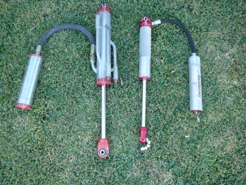 1988 Ford Bronco - Two off-road shock absorbers with remote reservoirs are shown on a grassy surface. One reservoir has visible text.