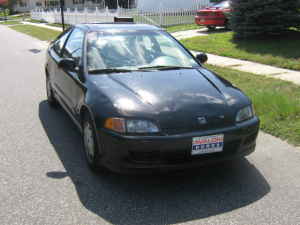 1996 Dodge 1500 - A black coupe is parked on the side of the road, with a red car visible in the background.