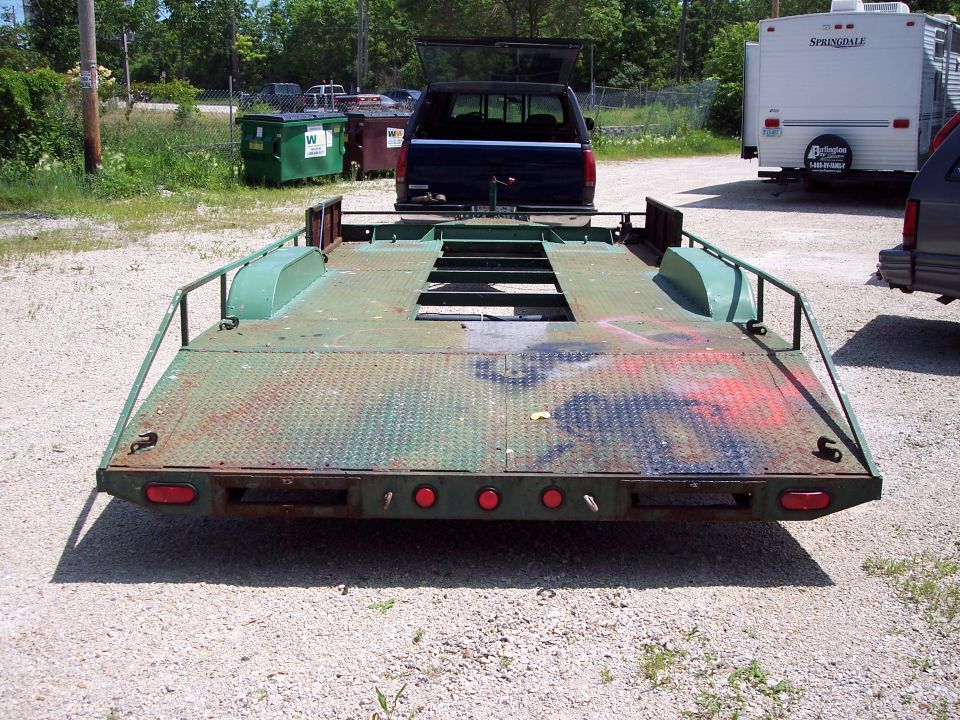 car hauler trailer with a dark blue pickup truck hitched to it, parked near dumpsters and a travel trailer
