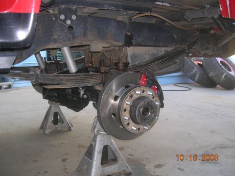 1985 Ford Bronco - The rear axle and suspension system, including leaf springs and disc brakes, are visible while the vehicle is supported by jack stands.