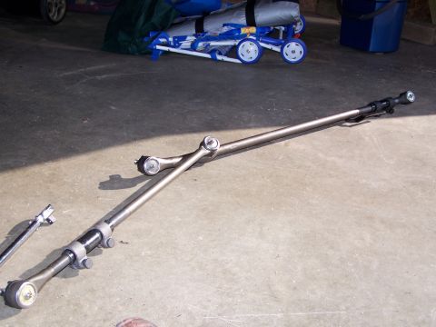 1986 Ford Bronco - New steering linkage laid out on a garage floor: a drag link and tie rod assembly with fresh tie rod ends, adjusting sleeves and clamps, al…