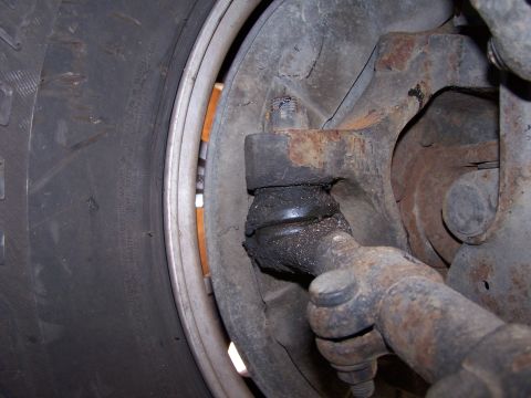 1986 Ford Bronco - Tight shot behind the wheel and tire at a worn tie rod end and its stud pressed into the rusty steering knuckle arm, with the castle nut re…