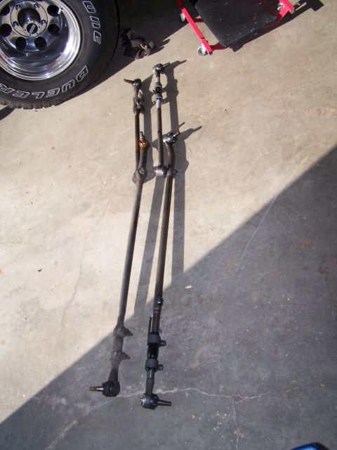 1986 Ford Bronco - Two steering linkage assemblies are shown on a concrete floor next to a tire.