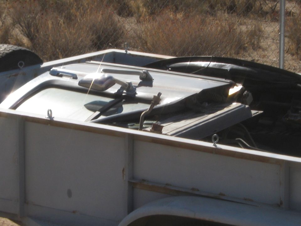 Trailer carrying a vehicle with a visible windshield and side mirror.