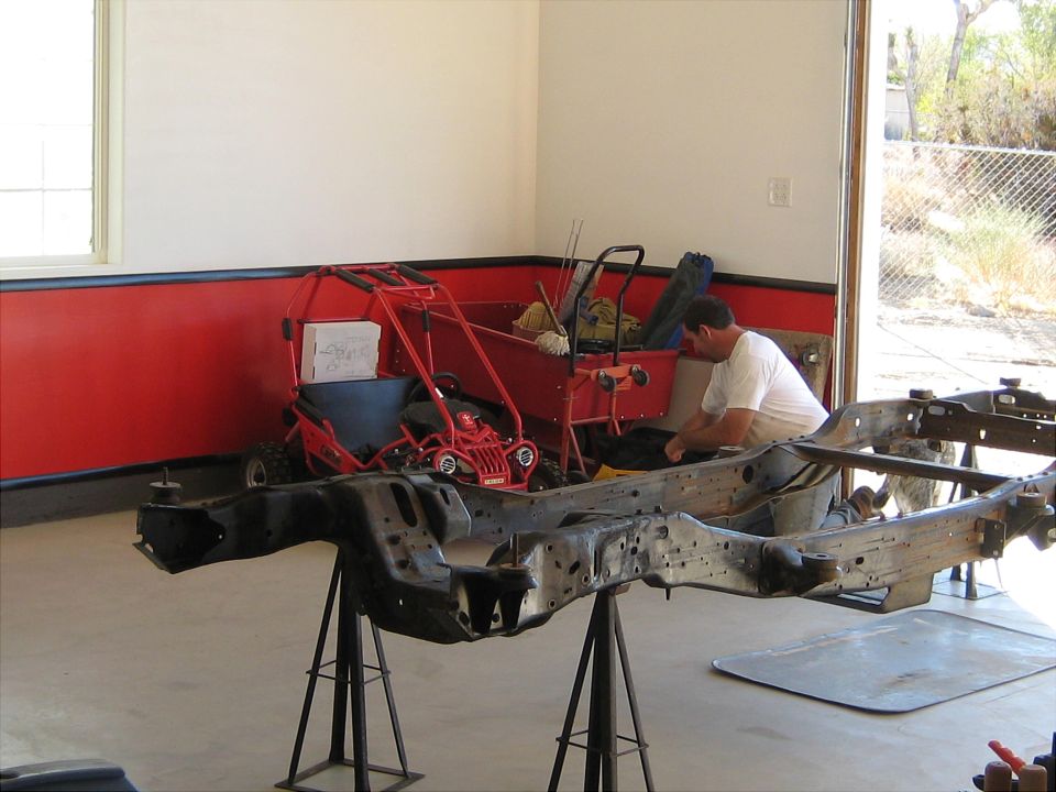 Vehicle frame being worked on in a garage with a go-kart in the background.