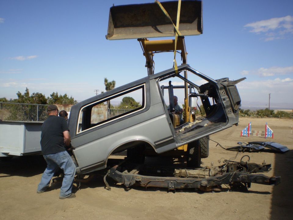 Forklift lifting SUV body off chassis with two men assisting