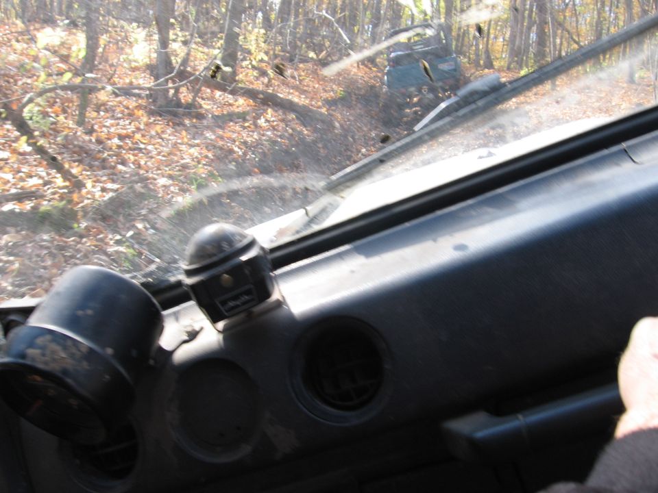 View from inside a vehicle looking out the windshield at another vehicle in a forest.