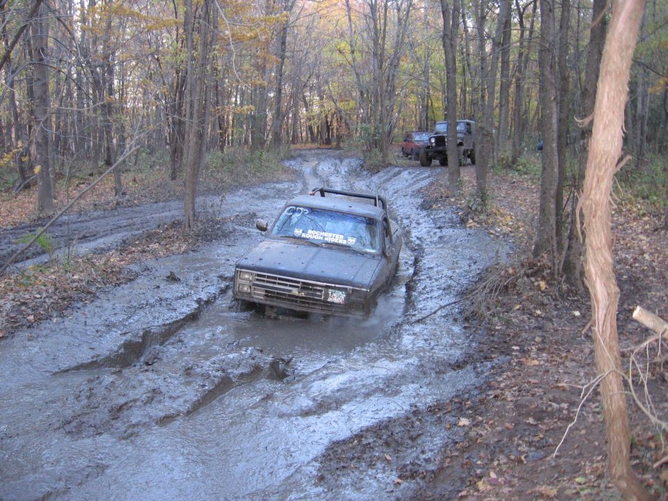 Pickup truck stuck in a deep mud pit on a wooded trail