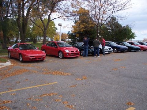 1996 Ford Probe - A line of cars parked in a lot with fallen leaves on the ground. The closest car is a red Ford Probe, followed by a red Dodge Neon, and sev…