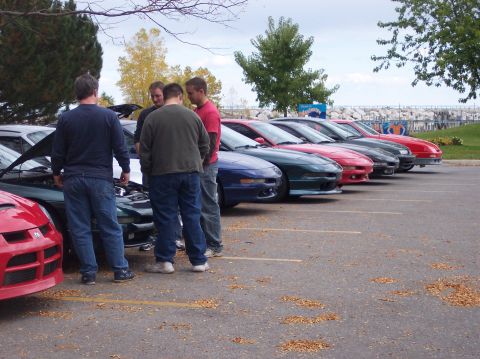 1996 Ford Probe - Four men stand around a dark green Ford Probe with its hood open, parked in a lot with other similar cars. A red car is visible in the fore…