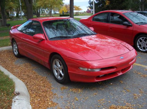 1996 Ford Probe - A red Ford Probe is parked on an asphalt lot covered with fallen leaves. Another red sedan is parked behind it.