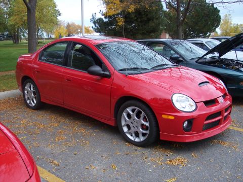 1996 Ford Probe - A bright red Dodge Neon sedan is parked on asphalt with fallen leaves scattered around. The car is viewed from the front three-quarter angl…