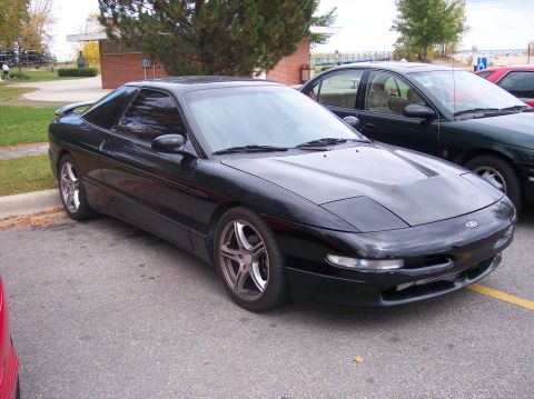1996 Ford Probe - A black 1996 Ford Probe is parked on asphalt next to a dark green sedan. The car is viewed from the front three-quarter angle, showing its…
