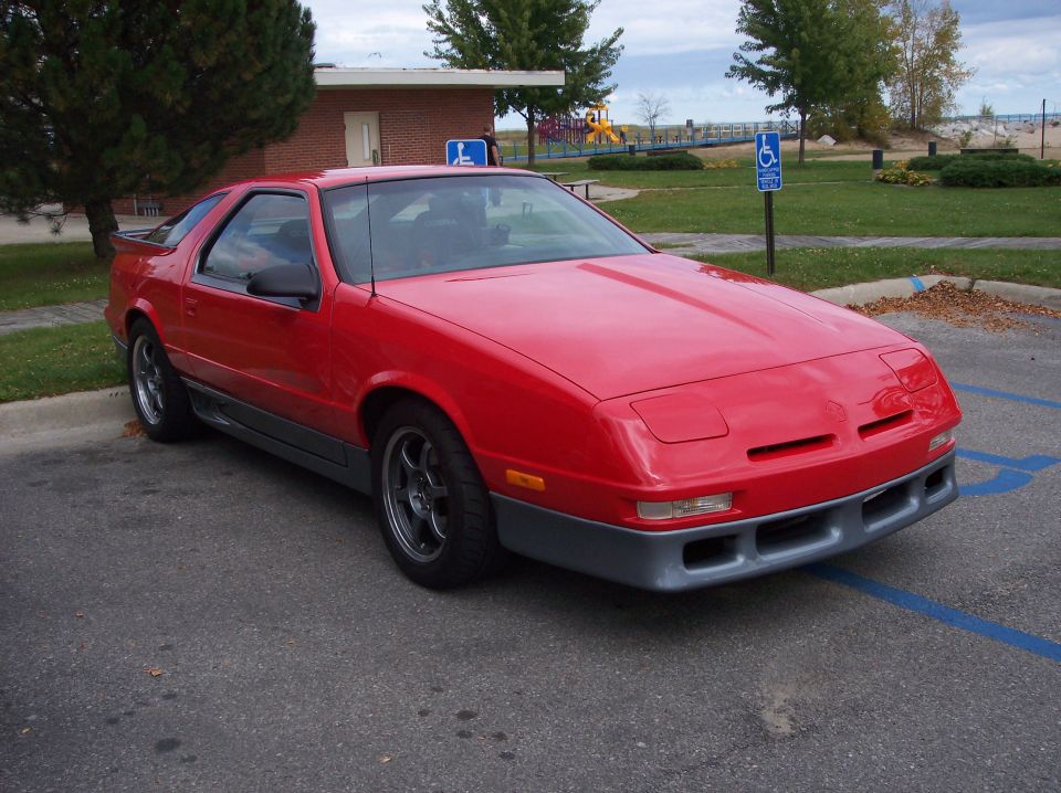 Red Dodge Daytona coupe with gray lower body kit and aftermarket wheels parked in a lot.