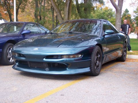 1996 Ford Probe - A dark teal 1996 Ford Probe is parked on asphalt with a yellow line marking a parking space. Another blue car is partially visible behind i…