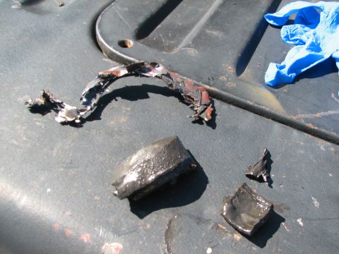 1979 Ford Bronco - Several pieces of damaged, melted metal and a blue glove are scattered on a dark, textured surface.