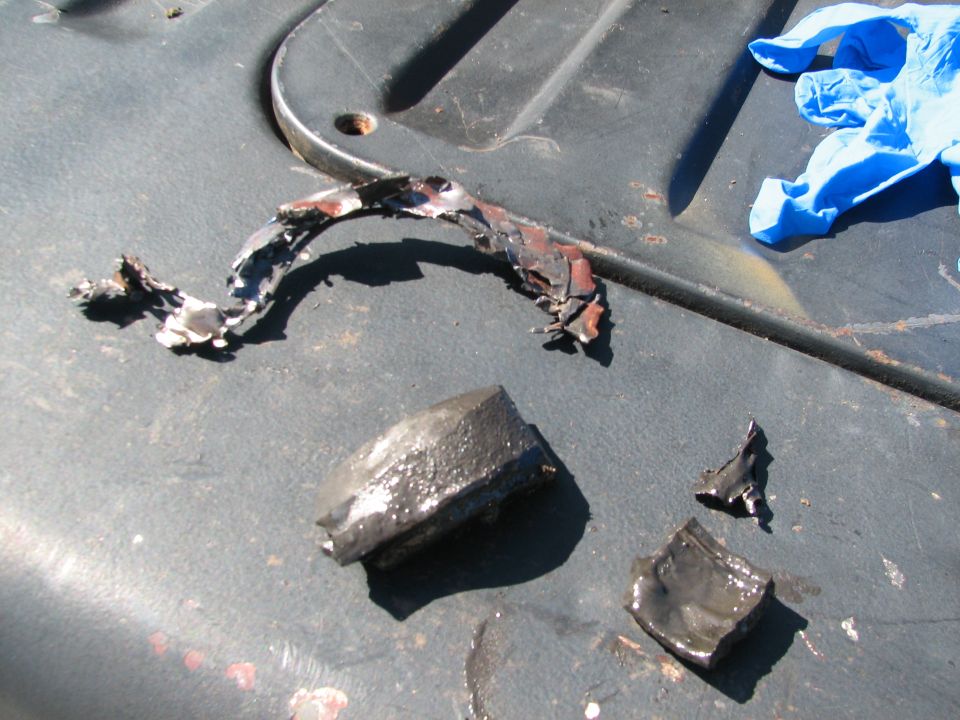 Melted metal debris and a blue glove on a dark surface.