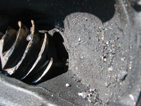 1979 Ford Bronco - Macro shot inside a failed gear case showing broken helical ring-gear teeth with chipped and cracked edges, next to a heavy coating of meta…