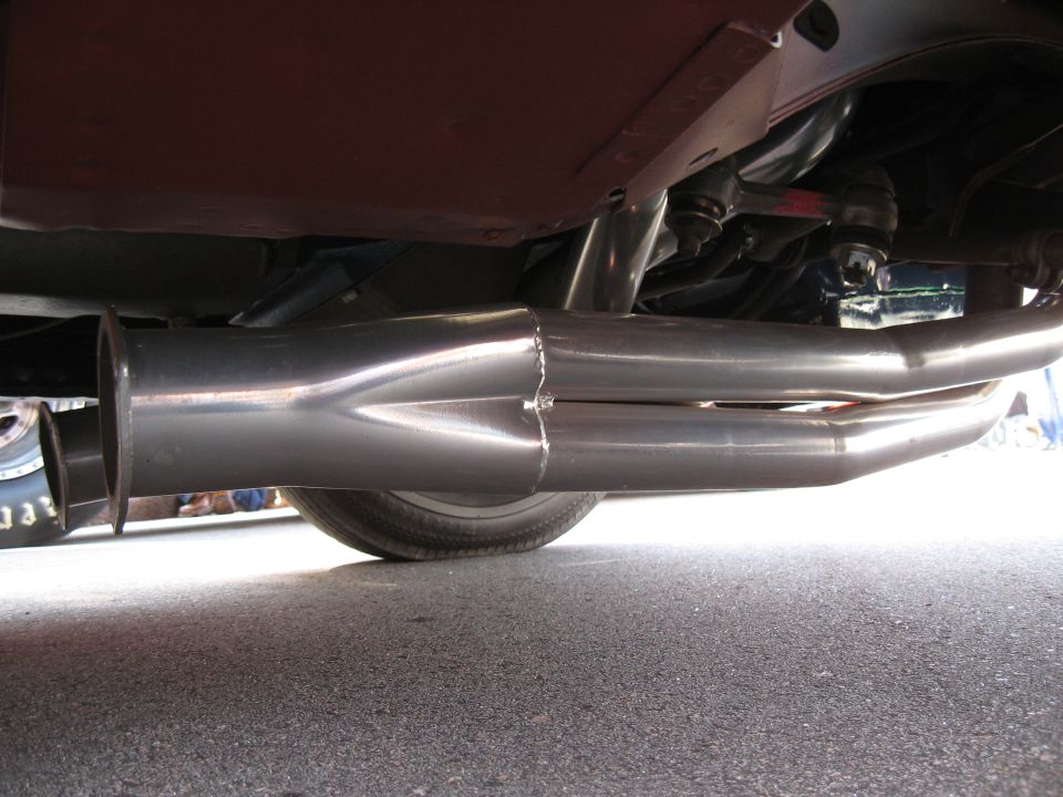 Underside of a vehicle showing a polished stainless steel dual exhaust system merging into one pipe.